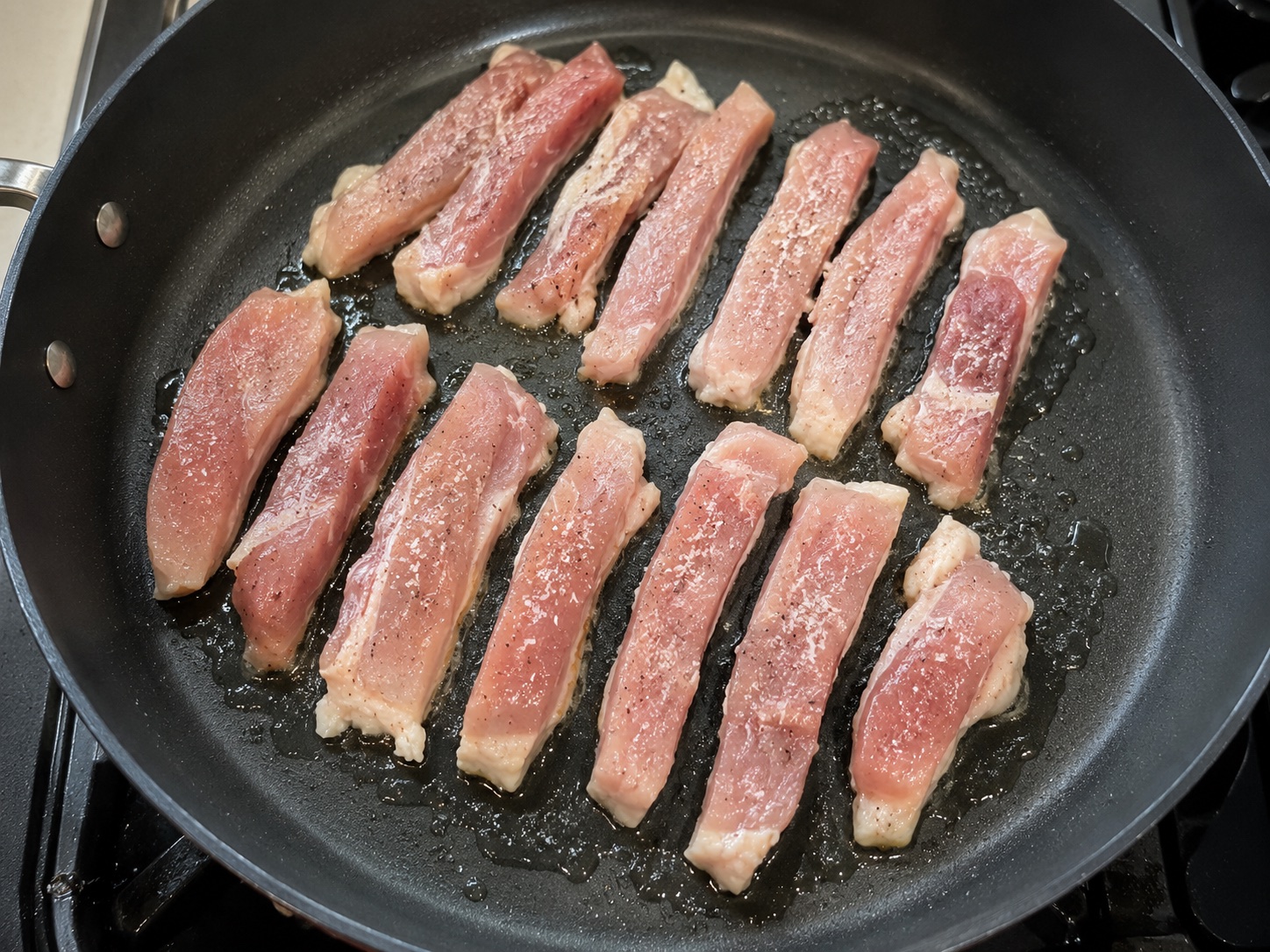 Chicken thigh strips arranged in one layer in a lightly oiled nonstick skillet